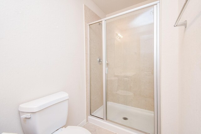 bathroom featuring toilet, an enclosed shower, and tile patterned flooring