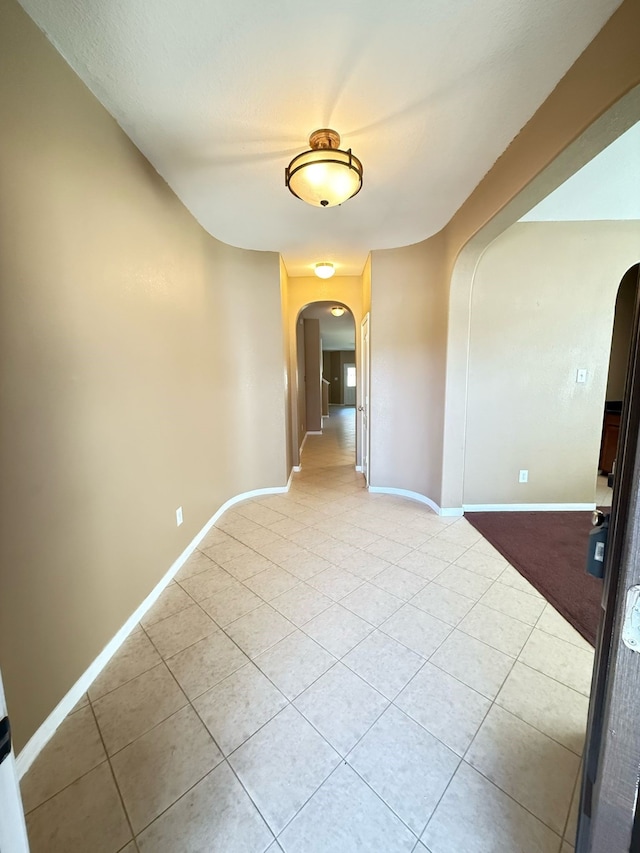 unfurnished room with arched walkways, light tile patterned floors, and baseboards