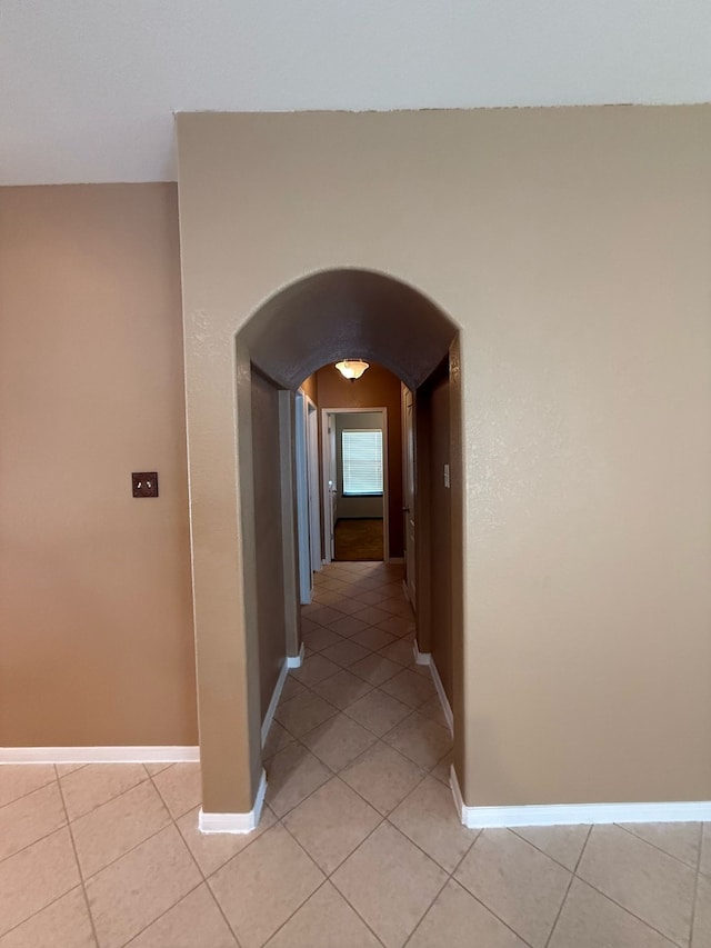 corridor with light tile patterned floors, baseboards, and arched walkways