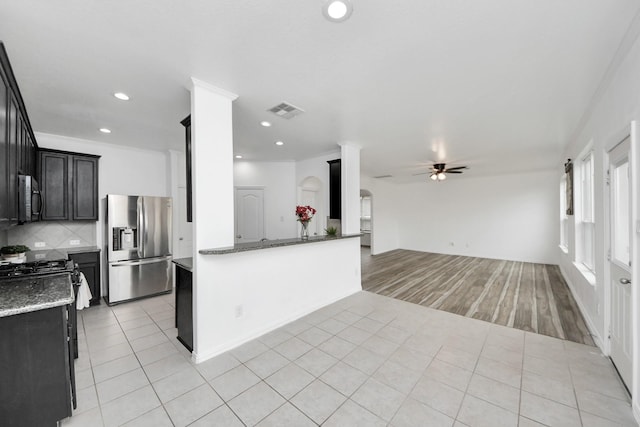 kitchen featuring ceiling fan, light tile patterned floors, decorative backsplash, dark stone countertops, and stainless steel appliances