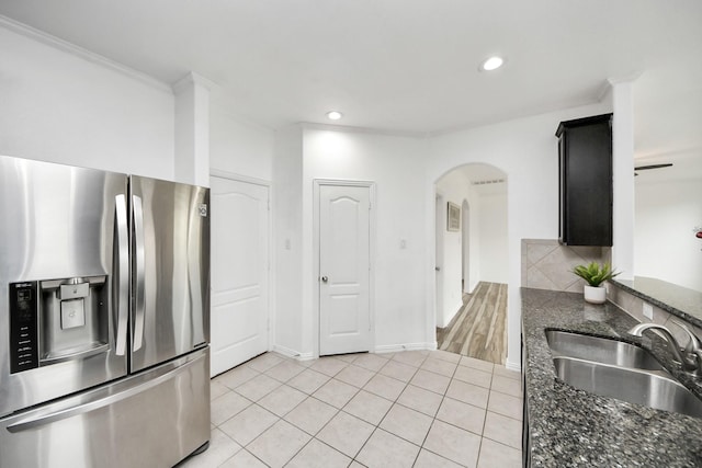 kitchen featuring stainless steel refrigerator with ice dispenser, dark stone counters, tasteful backsplash, sink, and light tile patterned floors