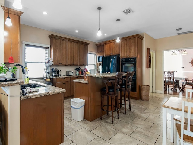 kitchen featuring a center island, pendant lighting, light stone counters, a breakfast bar, and black appliances