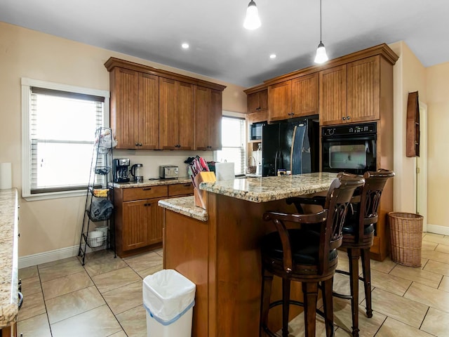 kitchen featuring black appliances, a center island, light stone countertops, and pendant lighting