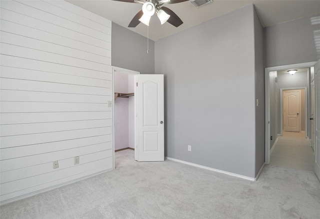 unfurnished bedroom featuring ceiling fan, light colored carpet, a spacious closet, and a towering ceiling