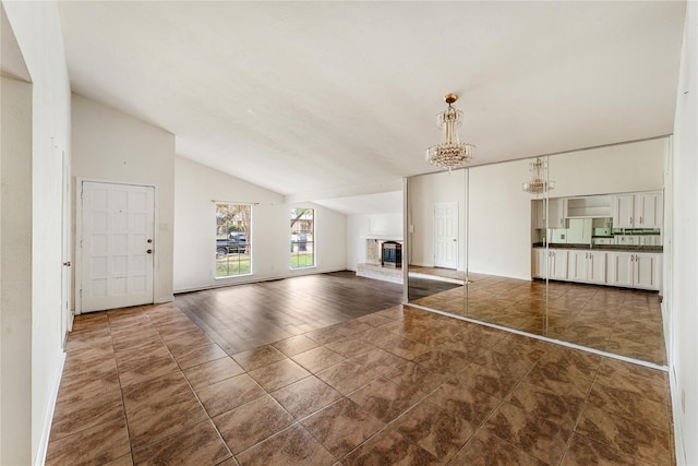 unfurnished living room featuring vaulted ceiling, dark tile patterned flooring, and an inviting chandelier