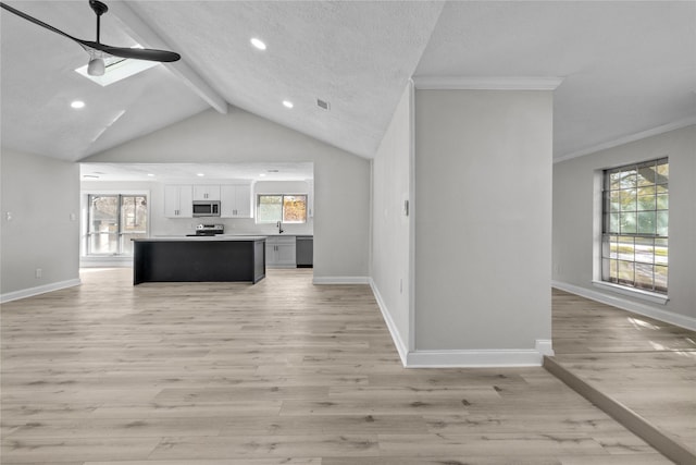 kitchen featuring vaulted ceiling with beams, white cabinetry, light wood-type flooring, appliances with stainless steel finishes, and a textured ceiling