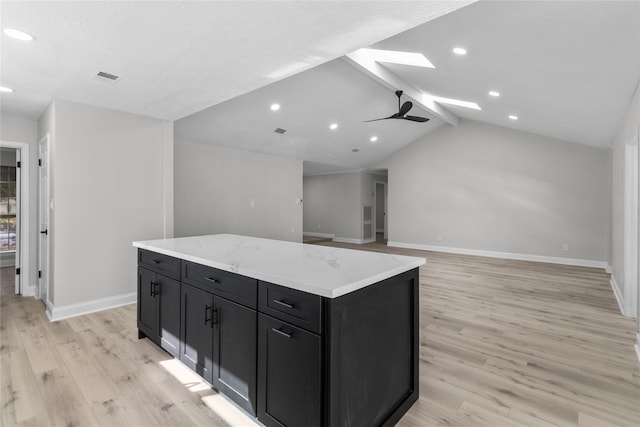 kitchen featuring light stone countertops, a center island, light wood-type flooring, ceiling fan, and lofted ceiling with skylight