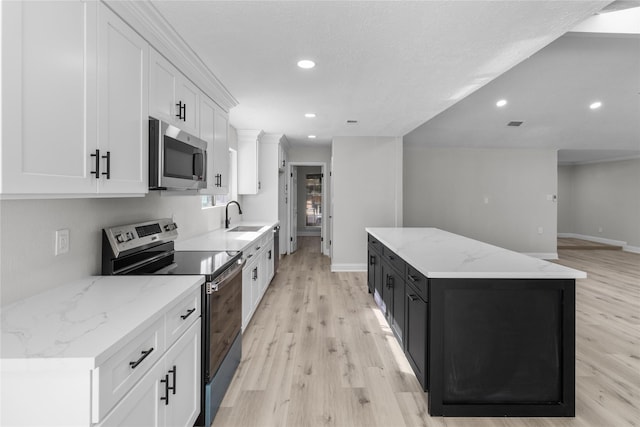 kitchen featuring a kitchen island, sink, white cabinetry, light stone countertops, and appliances with stainless steel finishes