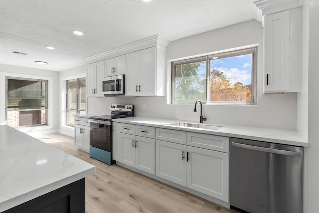 kitchen featuring sink, light wood-type flooring, appliances with stainless steel finishes, a textured ceiling, and white cabinets