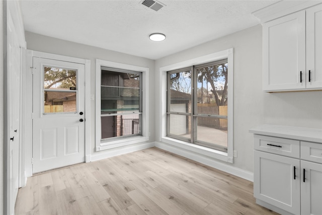 unfurnished dining area featuring light wood-type flooring and a textured ceiling