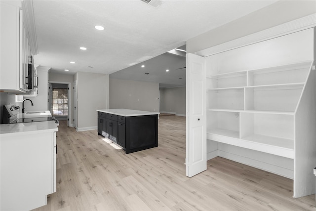 kitchen with white cabinets, sink, light hardwood / wood-style flooring, and a center island