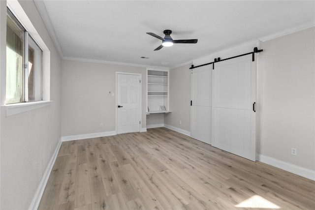 unfurnished bedroom featuring light wood-type flooring, ceiling fan, crown molding, and a barn door