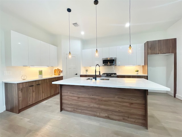 kitchen with decorative light fixtures, sink, white cabinets, and an island with sink