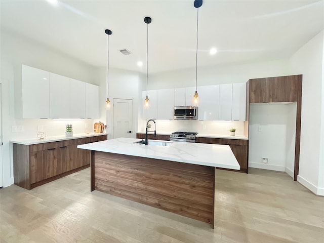 kitchen with appliances with stainless steel finishes, a kitchen island with sink, pendant lighting, white cabinets, and sink