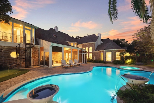 pool at dusk featuring a patio area, a sunroom, and an in ground hot tub