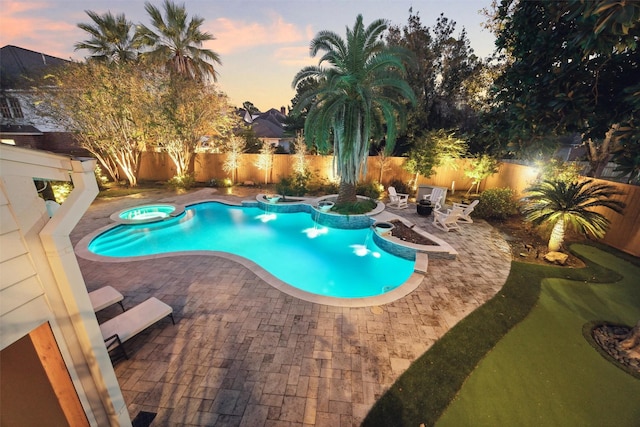 pool at dusk featuring a patio area and an in ground hot tub