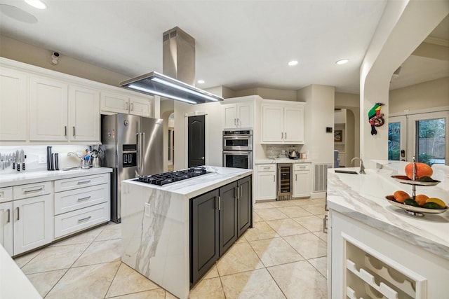 kitchen with white cabinetry, light stone counters, island range hood, appliances with stainless steel finishes, and a kitchen island