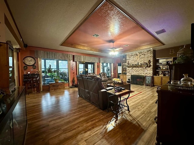 living room with ceiling fan, a textured ceiling, a raised ceiling, and hardwood / wood-style floors