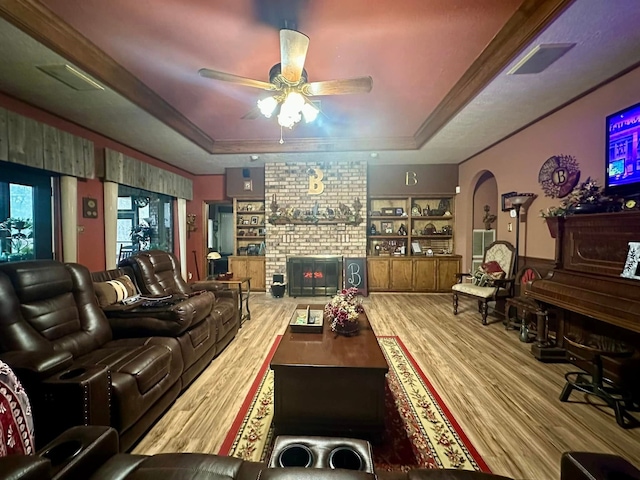 living room with built in shelves, a fireplace, hardwood / wood-style flooring, a raised ceiling, and ceiling fan