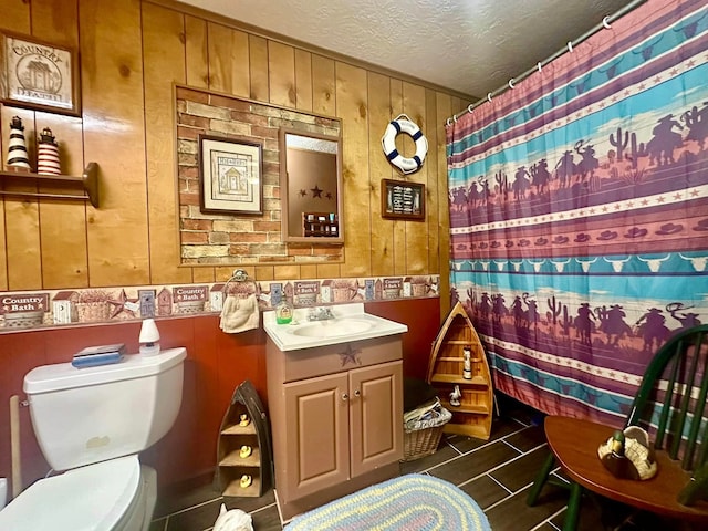 bathroom featuring toilet, vanity, wood walls, a textured ceiling, and curtained shower