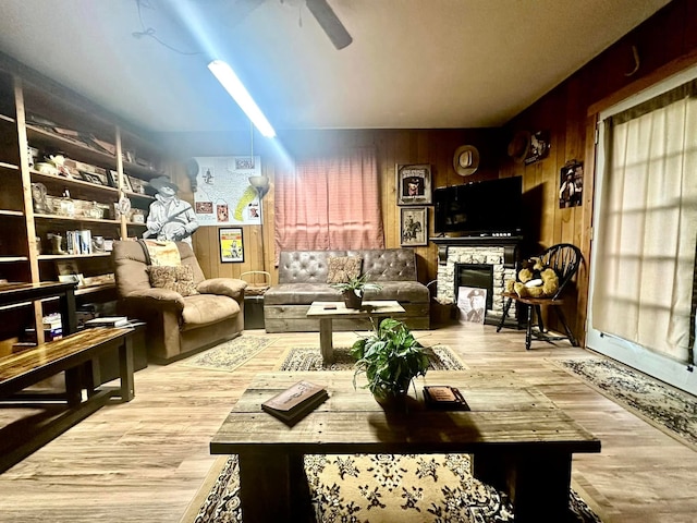 interior space with wooden walls, ceiling fan, light hardwood / wood-style flooring, and a stone fireplace