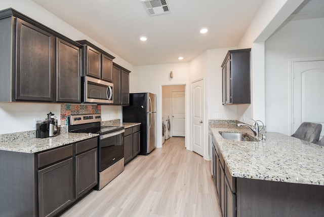 kitchen featuring light stone countertops, appliances with stainless steel finishes, washing machine and clothes dryer, sink, and light hardwood / wood-style flooring