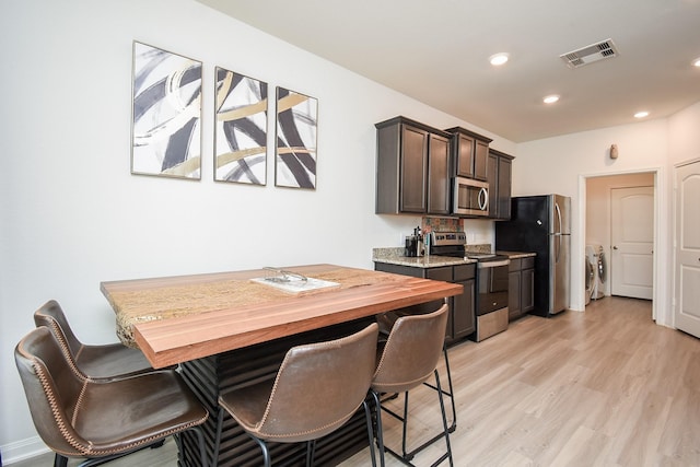 kitchen with washer and dryer, light stone countertops, appliances with stainless steel finishes, and light wood-type flooring