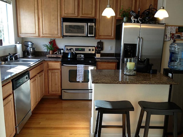 kitchen featuring decorative light fixtures, a breakfast bar area, stainless steel appliances, a sink, and light wood-type flooring