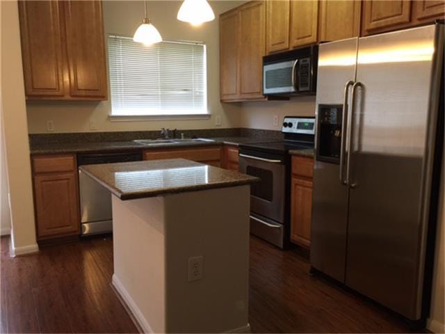 kitchen featuring a sink, appliances with stainless steel finishes, a center island, dark wood-style floors, and dark countertops