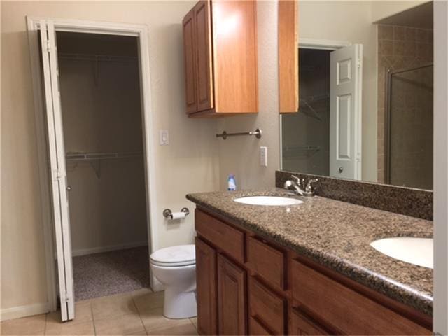 full bath featuring double vanity, toilet, a sink, a shower stall, and tile patterned floors