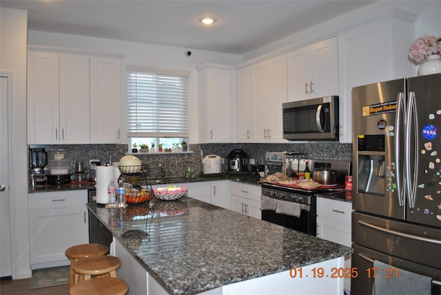 kitchen featuring backsplash, a kitchen island, white cabinetry, appliances with stainless steel finishes, and dark stone counters