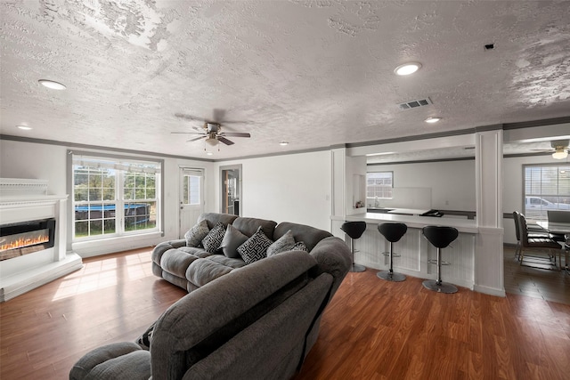 living room with a textured ceiling, ceiling fan, crown molding, and hardwood / wood-style flooring