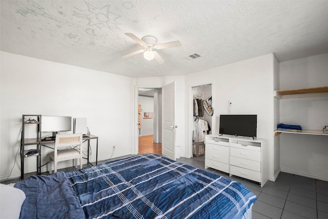 tiled bedroom featuring a spacious closet, ceiling fan, a closet, and a textured ceiling