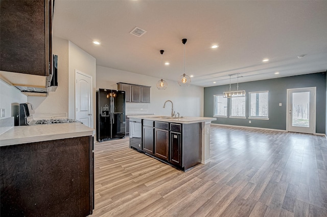 kitchen featuring dishwasher, black refrigerator with ice dispenser, decorative light fixtures, sink, and a kitchen island with sink