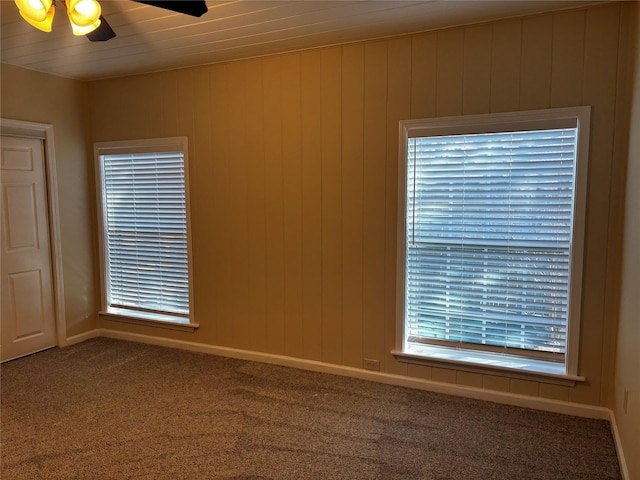 carpeted empty room with ceiling fan and wood walls