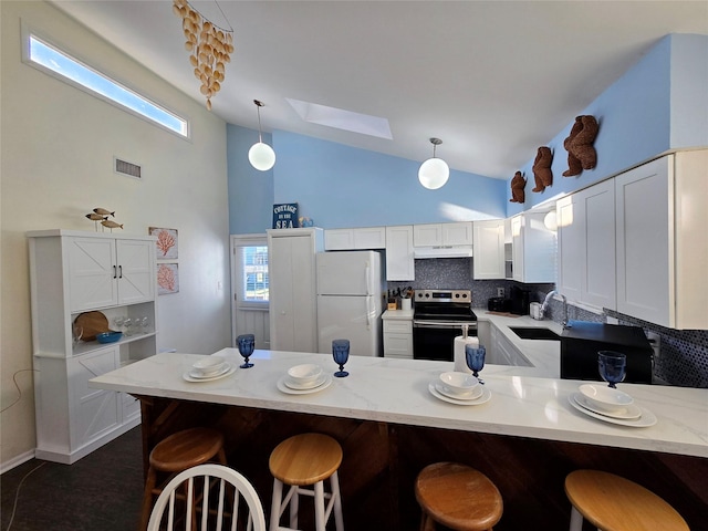 kitchen with vaulted ceiling with skylight, tasteful backsplash, decorative light fixtures, white refrigerator, and stainless steel electric stove