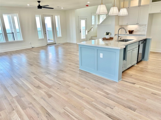 kitchen featuring decorative light fixtures, sink, backsplash, light wood-type flooring, and stainless steel dishwasher