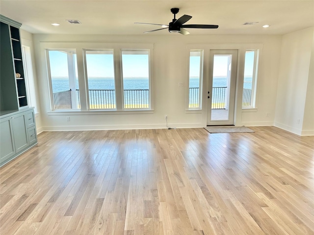 empty room with light wood-type flooring, ceiling fan, and a water view