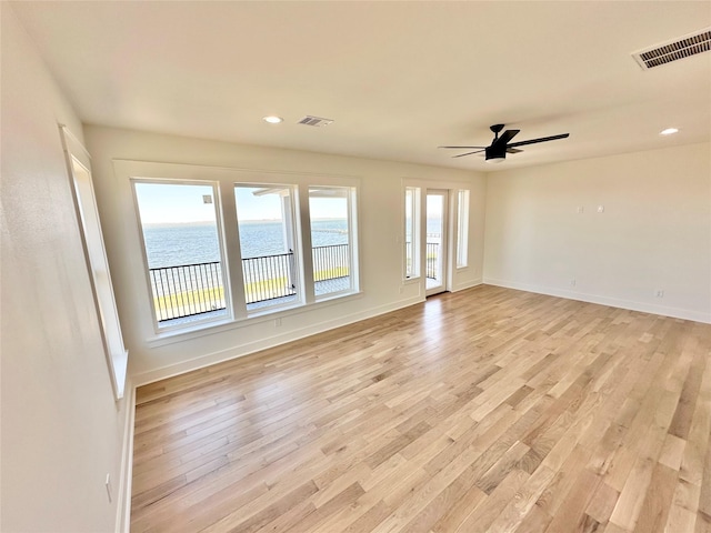 unfurnished room with ceiling fan, light hardwood / wood-style flooring, and a water view