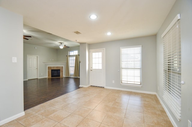 unfurnished living room with light tile patterned flooring, ceiling fan, and a tiled fireplace