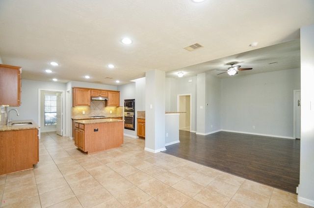 kitchen with light tile patterned flooring, a kitchen island, appliances with stainless steel finishes, sink, and backsplash