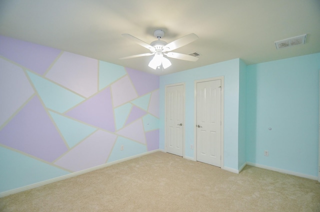 unfurnished bedroom featuring ceiling fan, light carpet, and two closets