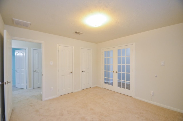 unfurnished bedroom featuring light carpet, french doors, and a textured ceiling