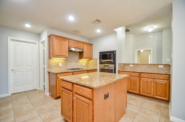 kitchen with a kitchen island, tasteful backsplash, light tile patterned floors, stainless steel appliances, and light stone countertops