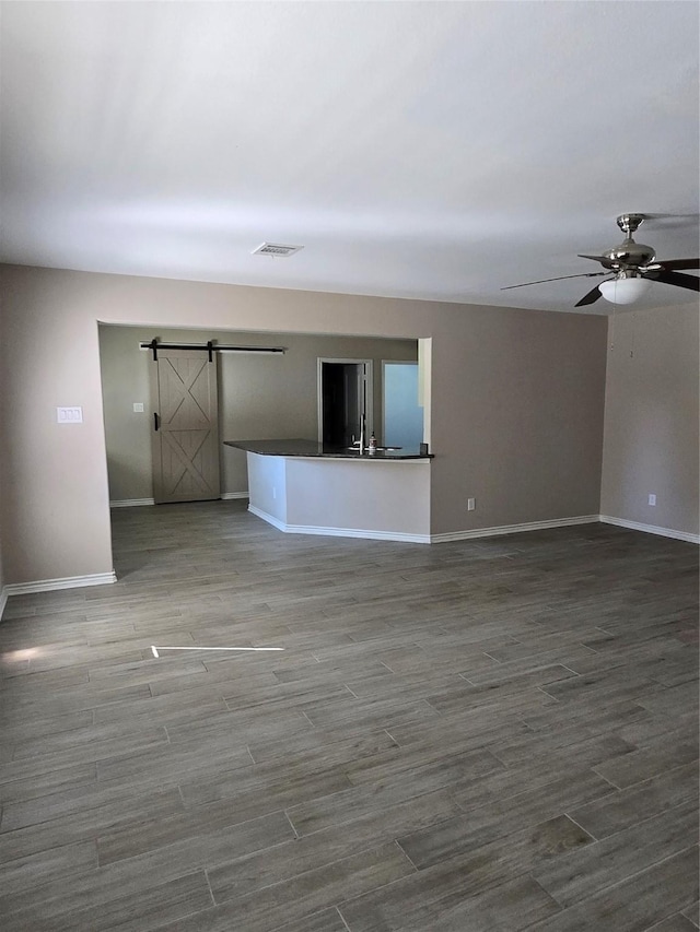 unfurnished living room with ceiling fan and a barn door