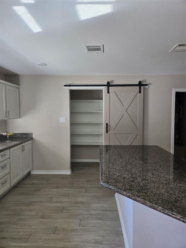 kitchen featuring a barn door, dark stone counters, and white cabinetry