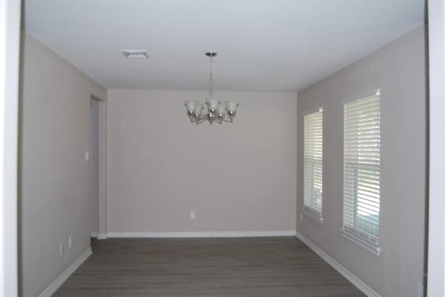 spare room with a wealth of natural light, dark hardwood / wood-style flooring, and an inviting chandelier