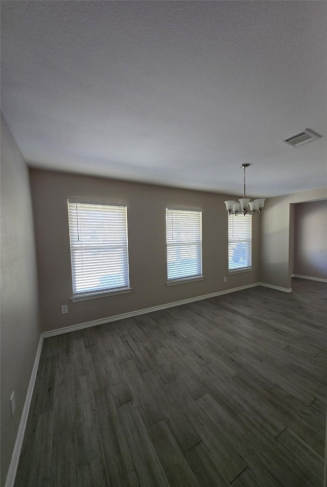 unfurnished room featuring a notable chandelier, dark hardwood / wood-style flooring, and a textured ceiling