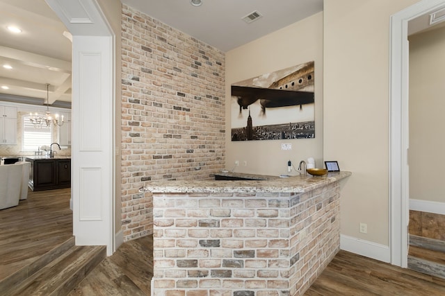 bar with dark hardwood / wood-style floors, pendant lighting, sink, an inviting chandelier, and light stone countertops