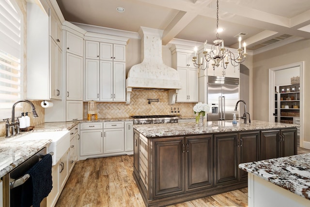 kitchen with light hardwood / wood-style floors, stainless steel appliances, a kitchen island with sink, dark brown cabinets, and custom range hood